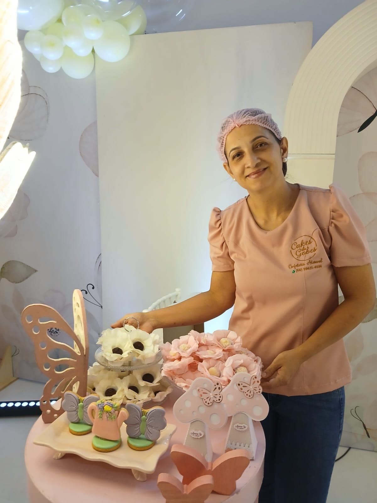 Francieli, a confeiteira, sorrindo ao lado de uma mesa de doces